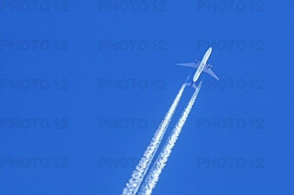 Flying twin-engine jet airliner, aircraft, plane from the airline Kuwait Airways showing contrails, condensation trails against blue sky