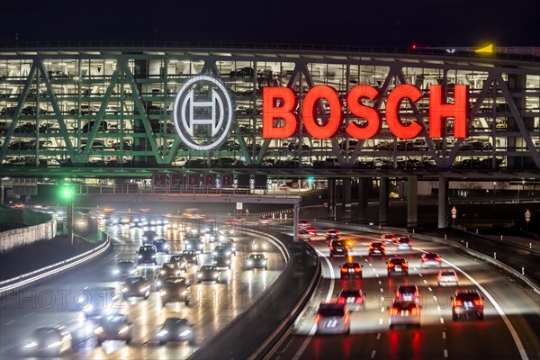 A8 motorway at Stuttgart Airport with Bosch multi-storey car park in the evening, cars create light trails. The 440 metre long construction offers space for 4200 vehicles. Bosch owns the naming rights, the stylised ignition anchor measures 12 metres in diameter. This makes it one of the largest neon signs in the world. Stuttgart, Baden-Wuerttemberg, Germany, Europe
