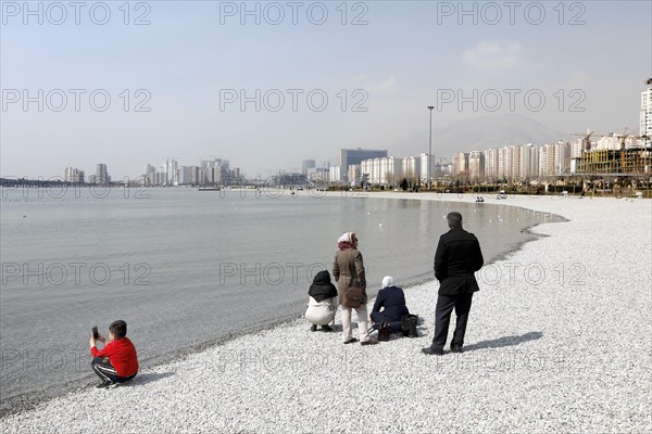 A family on the beach of Lake Chitgar in Tehran, Iran. Lake Chitgar is a man-made lake in the north-west of Tehran, also known as the Lake of the Martyrs of the Persian Gulf, 10 March 2019
