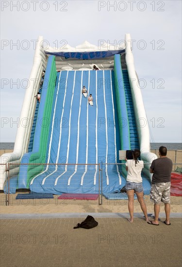 Children playing on giant inflated slide seaside attraction, Great Yarmouth, Norfolk, England parents watching using computer tablet to take photos