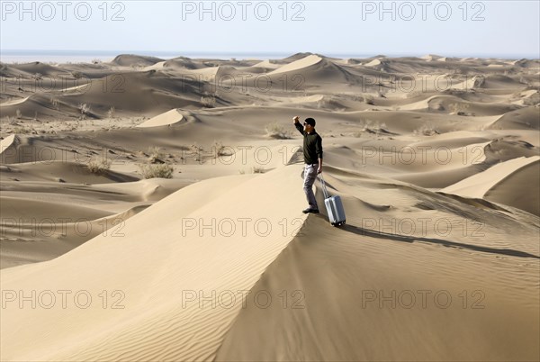 Symbolic image, tourist with suitcase in the desert, Mesr Desert, Iran. The Mesr Desert is part of the central Dashte-Kavir desert, 12.03.2019