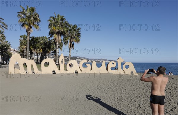 A man takes a photo of a large Malagueta logo. Malagueta is the name of the beach in Malaga, on the Costa del Sol, 11/02/2019