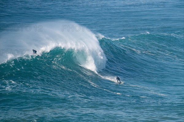 Two surfers ride a crashing wave at the same time, Nazare, Portugal, Europe