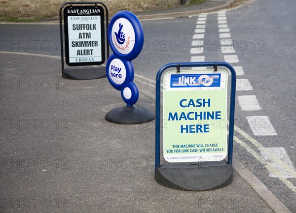 ATM sign outside shop with newspaper headline warning of scam taking place, Suffolk, England, United Kingdom, Europe