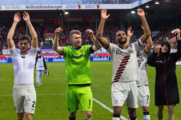 Football match, the Bayer Leverkusen players from left to right: Josip STANISIC, goalkeeper and captain Lukas HRADECKY, Jonathan TAH, Jonas HOFMAN hidden and Florian WIRTZ celebrate the victory with their travelling fans in the fan curve, Voith-Arena football stadium, Heidenheim