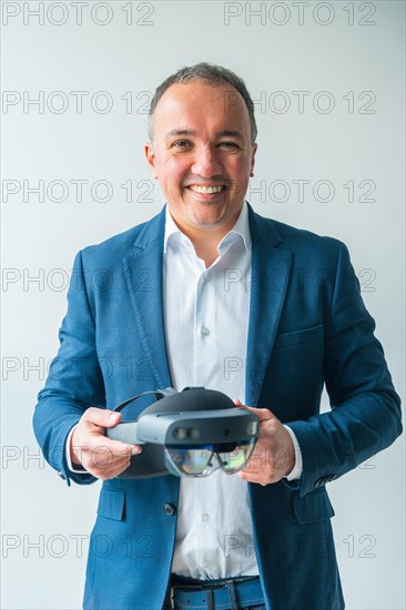 Vertical studio portrait with grey background of a confident businessman holding a futuristic mixed reality goggles