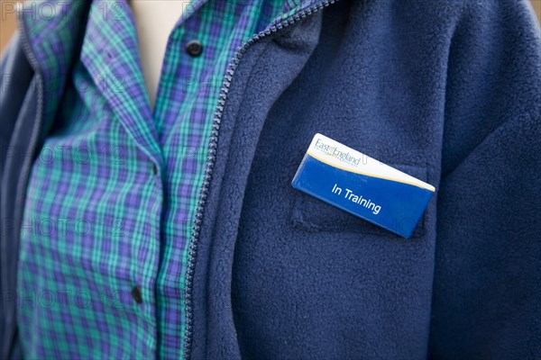 Model released teenage girl in uniform for her job in a Co-operative shop, UK wearing a badge saying 'In Training'