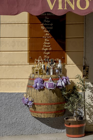 A wine barrel serves as a display area for bottles in front of a souvenir shop under warm sunlight, Porec, Istria, Croatia, Europe