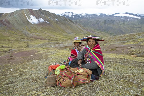 Peruvian woman, 55 and 27 years old, in traditional dress sit with an infant, 7 months old, in a field with the Cordillera de Colores or Rainbow Mountains in the background in Palccoyo, Checacupe district, Canchis province, Cusco region, Peru, South America