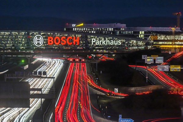 A8 motorway at Stuttgart Airport with Bosch multi-storey car park in the evening, cars create light trails. The 440 metre long construction offers space for 4200 vehicles. Bosch owns the naming rights, the stylised ignition anchor measures 12 metres in diameter. This makes it one of the largest neon signs in the world. Stuttgart, Baden-Wuerttemberg, Germany, Europe