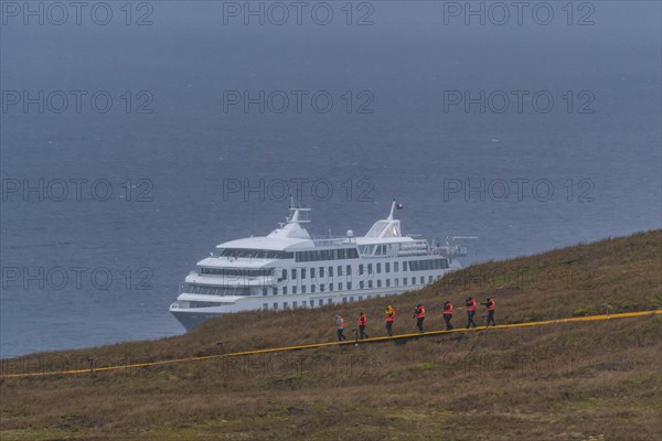 Passengers of the cruise ship Stella Australis in life jackets hike in storm and rain to Cape Horn, southernmost point of America, Horn Island, Cabo de Hornos National Park, Tierra del Fuego, Patagonia, Chile, South America