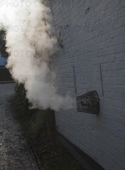 Heat steam emissions from domestic oil powered boiler heating system released through wall of house into the air