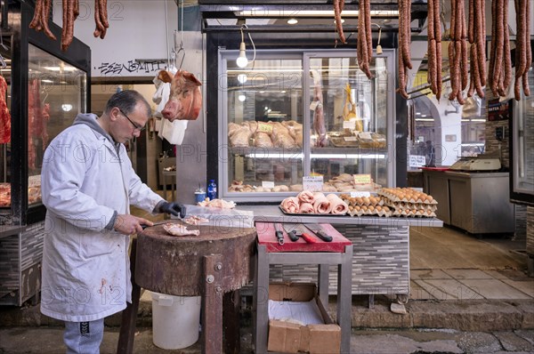 Butcher, meat trader cutting meat in front of his market stall, display of fresh meat, sausages, pork head, butchery, food, Kapani market, Vlali, Thessaloniki, Macedonia, Greece, Europe