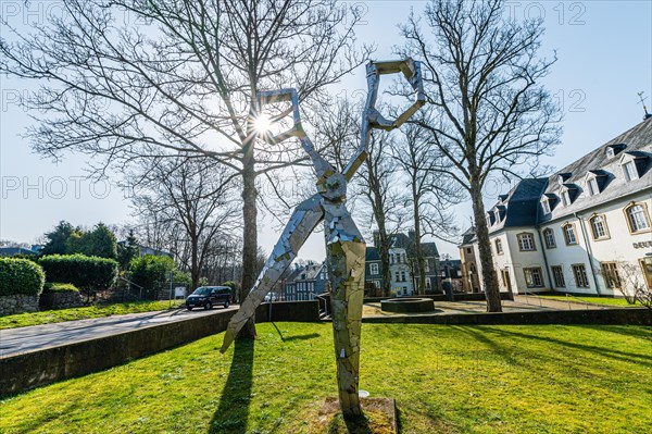 A modern metal sculpture in front of a castle, with the sun shining through its form, surrounded by trees on a clear day, Klingenmuseum, Graefrath, Solingen