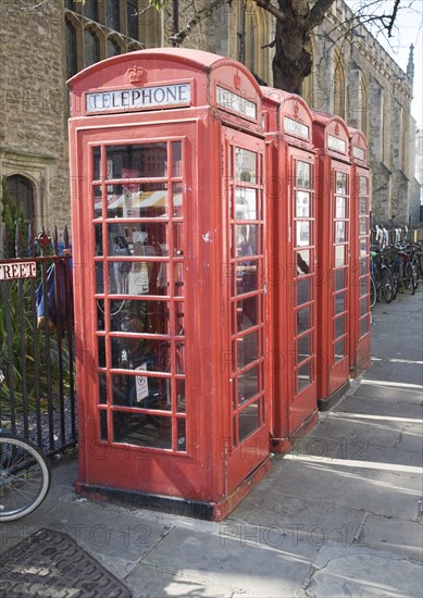 Four old red telephone boxes in the street, Cambridge, England woman walking into frame using a mobile phone