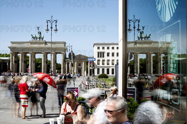 The Brandenburg Gate is reflected in a pane of glass. A long exposure shows tourists at Cafe am Brandenburg Gate, Berlin, 06.05.2018