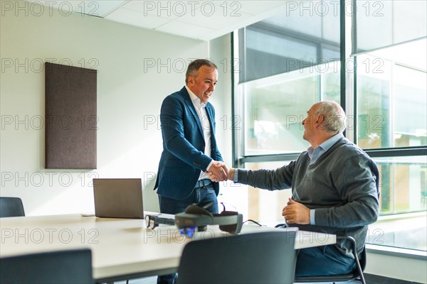 Business people shaking hands in the office next to futuristic goggles