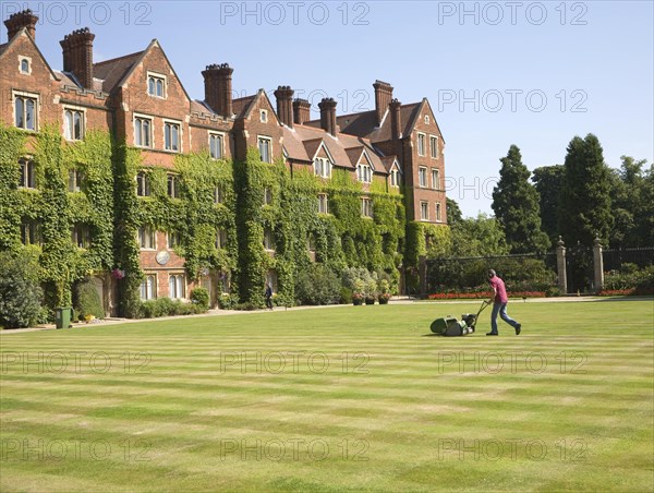 Man mowing grass lawn in courtyard of Selwyn College, University of Cambridge, England, United Kingdom, Europe