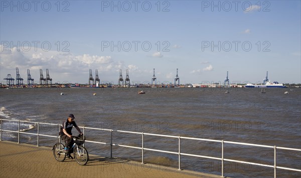 Man cycling on the seafront at Harwich, Essex, England with the Port of Felixstowe in the background