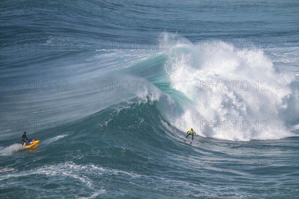 A jet ski and a surfer on a rolling wave, Nazare, Portugal, Europe