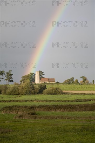The end of a rainbow lights up the tower of All Saints church, Ramsholt, Suffolk, England, United Kingdom, Europe