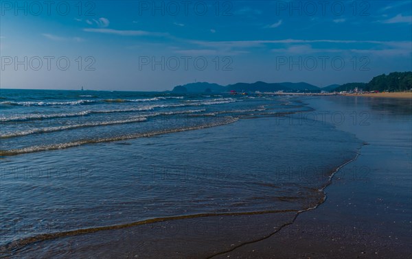 Gentle waves wash over sandy beach with clear blue sky, in South Korea
