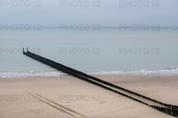 Grey breakwater juts out into a still sea, separating the wet from the dry sand