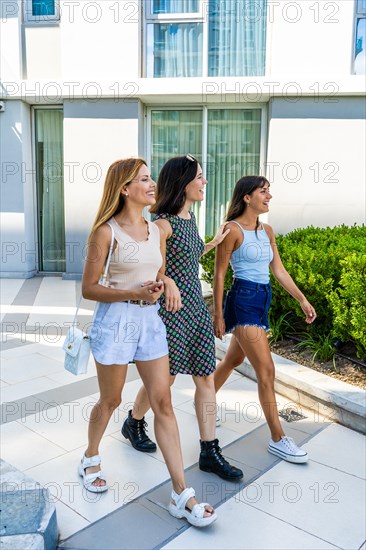 Three women are walking down a sidewalk, smiling and laughing