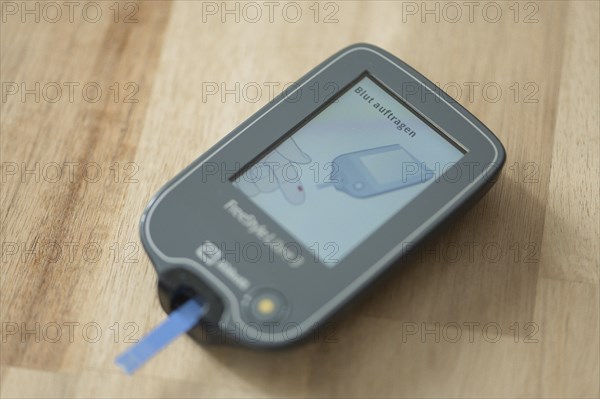Blood glucose meter with test strips lying diagonally in the centre on a wooden table, ready for a blood glucose measurement, diabetes treatment, glucose measurement, Ruhr area, Germany, Europe