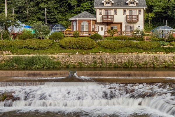 Elegant houses overlook a small cascading waterfall on the riverbank, in South Korea