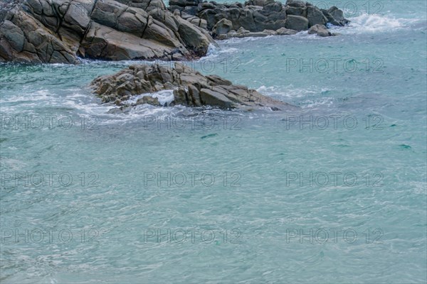 Foaming sea waves hit a rocky coast with a hint of green in the water, in South Korea