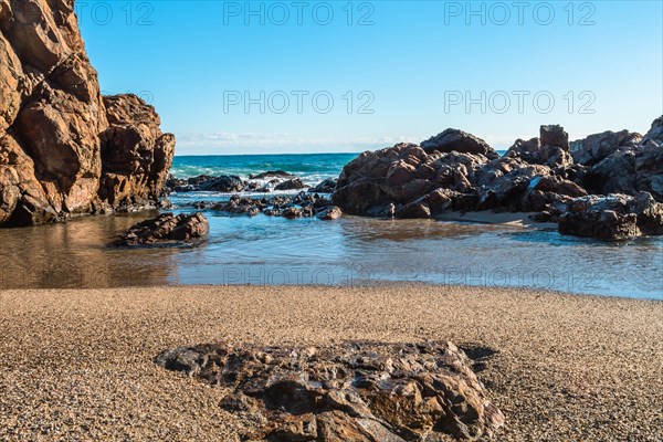 Sandy beach with large rocks and waves crashing in from the sea under a blue sky, in South Korea