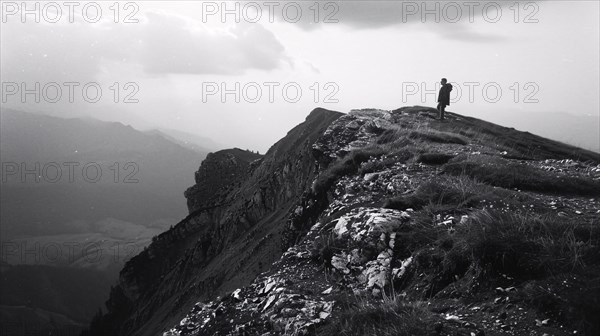 A hiker stands on a mountain peak surveying the surrounding rugged terrain, AI generated