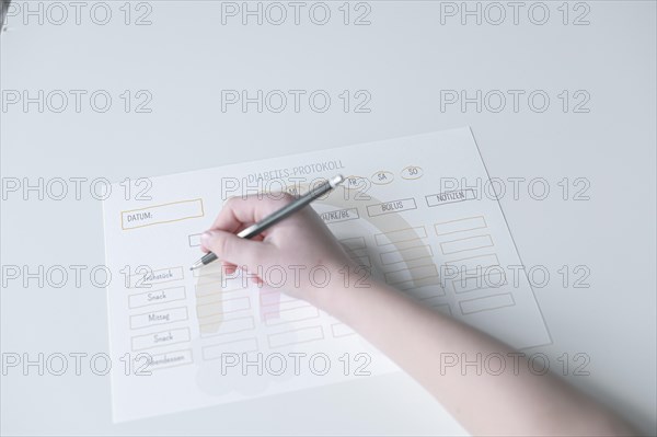 Diabetes log, daily log of food and insulin administration, food log, hand of a child holding a pen and appearing to fill in the log, the paper lies on a white table, Ruhr area, Germany, Europe