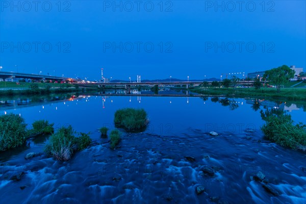 Pebbled riverfront reflecting bridge lights at twilight, in South Korea