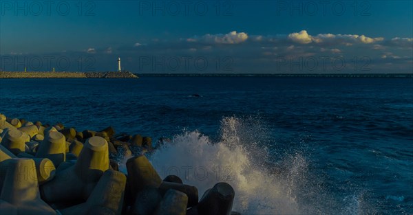 Evening view of a calm seashore with spray over tetrapods, lighthouse in the background, in South Korea