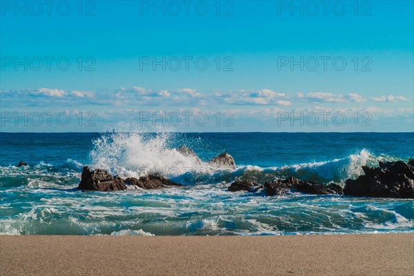 Spray rises as waves collide with rocky outcrops on a sandy beach, in South Korea