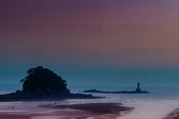 Silhouette of a lighthouse on a tranquil beach under a purple and orange sunset sky, in South Korea
