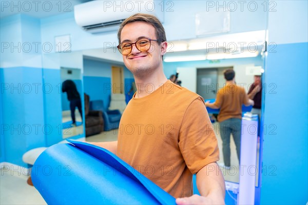 Happy and satisfied man with down syndrome after yoga class holing a mat