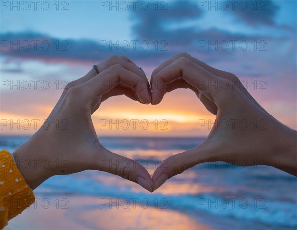 Two woman's hands form a heart in front of a colourful sky on the beach, AI generated, AI generated
