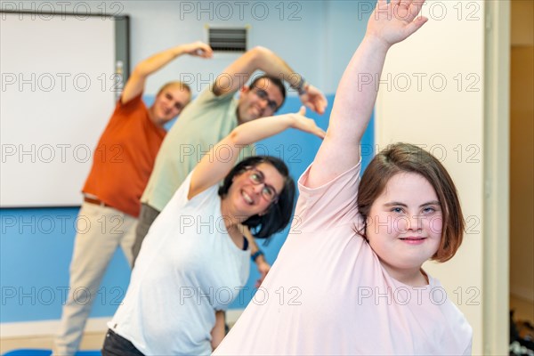 Focus on a woman with down syndrome and a group of people with special needs stretching in the gym