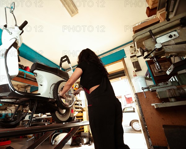 A focused female mechanic is at work on a scooter's tire in a workshop setting, latino woman in traditional masculine jobs concept, feminine power in real life