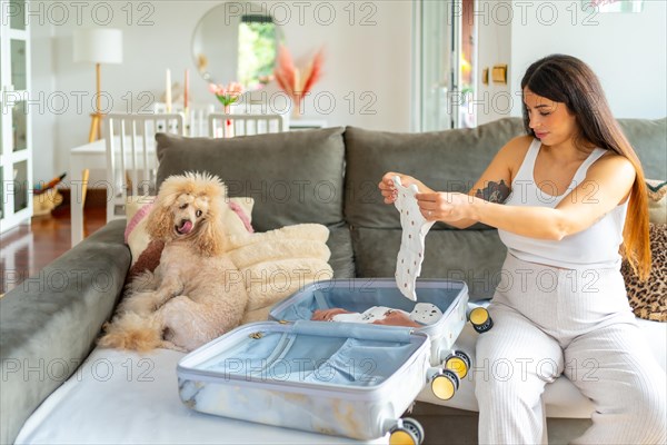 Pregnant woman preparing a suitcase to go to the hospital sitting on a sofa next to a dog