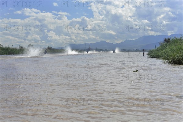 Speedboats create water fountains on a river with cloudy sky in the background, Inle Lake, Myanmar, Asia