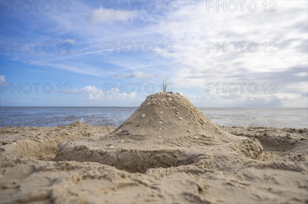 Sandcastle with shells and moat on the beach, in the background sea and blue sky, Schillig, Wangerland, North Sea, Germany, Europe