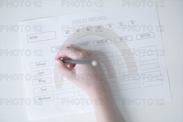 Diabetes log, daily log of food and insulin administration, food log, hand of a child holding a pen and appearing to fill in the log, the paper lies on a white table, Ruhr area, Germany, Europe