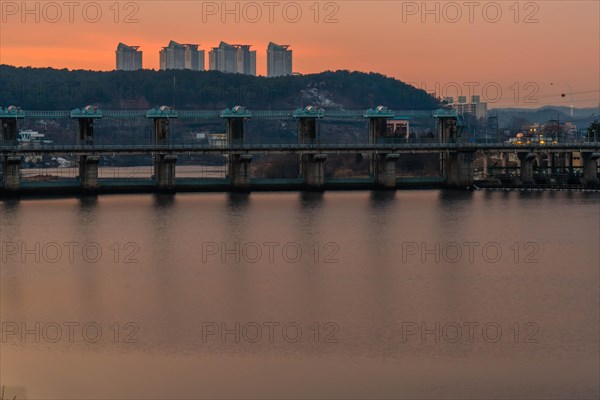 Golden hour sunset illuminating a dam on the river with buildings behind, in South Korea