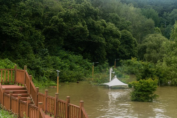 White awning over flooded river where picnic table has been submerged under water from monsoon rains in Daejeon South Korea