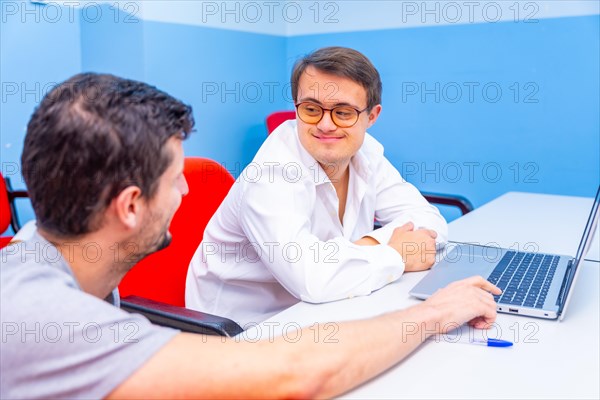 Happy and relaxed man with down syndrome and teacher talking during IT computing class