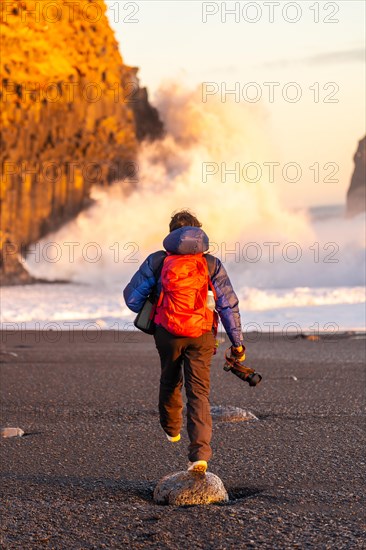 Adventurous photographer woman from behind in winter in Iceland visiting the Reynisfjara Black Sand Beach